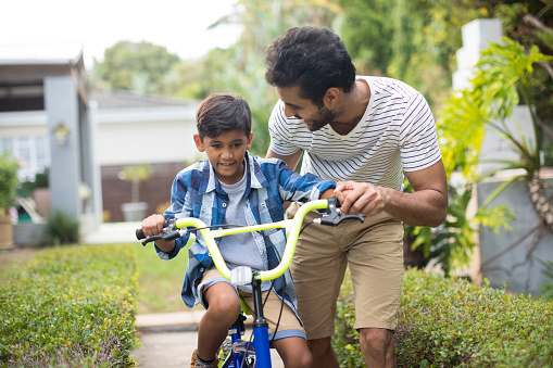 Man assisting son for cycling in yard