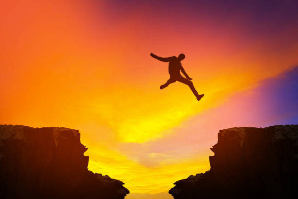 istock Man jumping over precipice between two rocky mountains at sunset 847923256