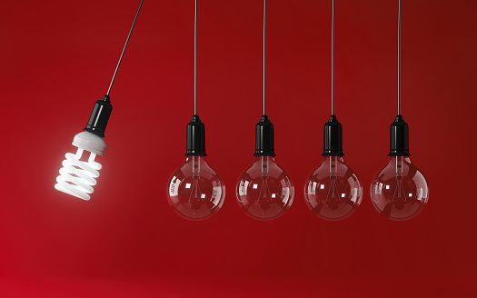 Energy saving light bulb in perpetual motion on red background. Energy efficiency concept. Horizontal composition with copy space.