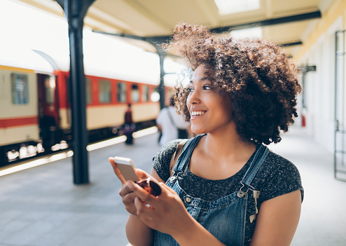 Smiling woman using smart phone on station, wears casual clothes.
