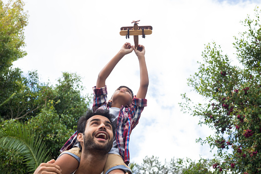 Low angle view of father carrying son playing with airplane in yard