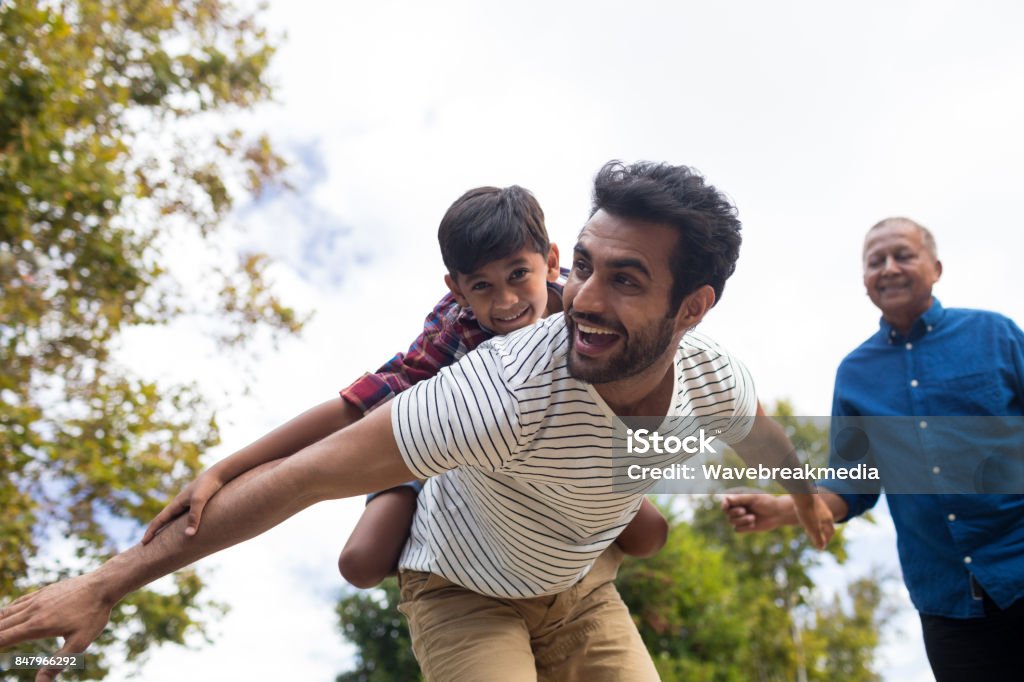 Happy grandfather looking at man giving piggy backing to son Happy grandfather looking at man giving piggy backing to son with arms oustretched in yard Family Stock Photo