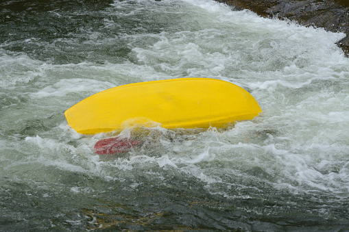 Upside down overturned kayak in white water rapids