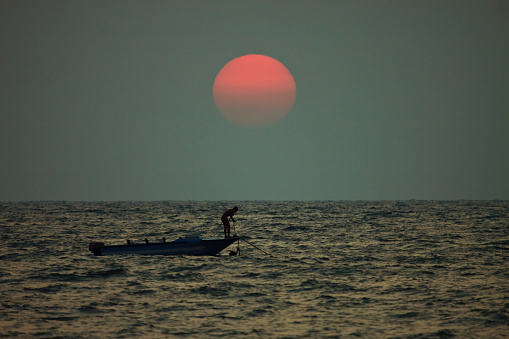 Panjim, GOA, India: Taken this picture off the coast of Goa at sunset of a skiff boat which was tied off the coast. Tried to capture the setting sun in the background and the skiff boat in foreground with the boat man standing there.