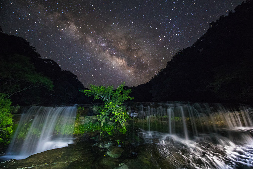 A clear night sky with the bright Milky way right above a waterfall on an island off Okinawa, Japan