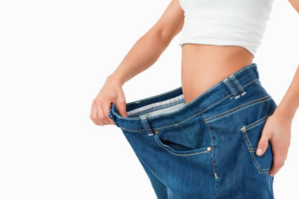 Fit woman wearing too large pants Fit woman wearing too large pants against a white background too thin stock pictures, royalty-free photos & images