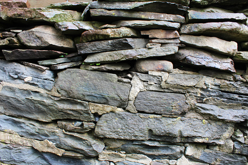 Rock wall made of both stacked and mortared irregular grey stones, horizontal view