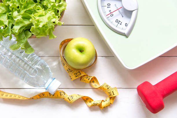 mela verde e scala di peso, misura il rubinetto con verdure fresche, acqua pulita e attrezzature sportive per la dieta femminile dimagrante.  dieta e concetto sano - apple women green eating foto e immagini stock