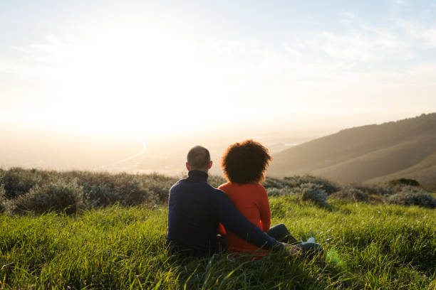 Couple sitting in a meadow and watching the sunset Photo of couple sitting in a meadow and watching the sunset arm around photos stock pictures, royalty-free photos & images