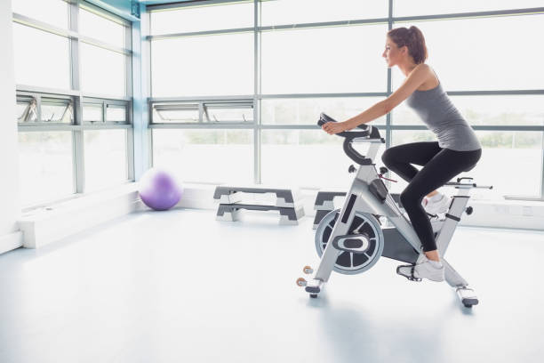 woman riding an exercise bike - spinning instructor exercising gym imagens e fotografias de stock