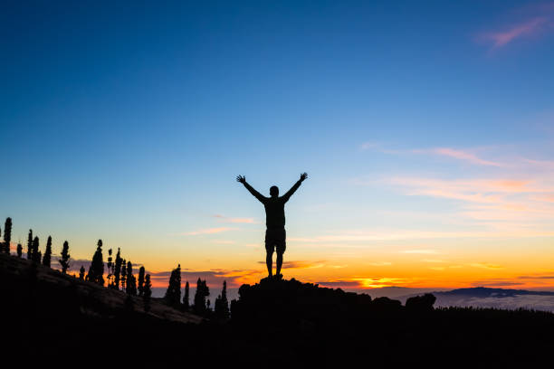 hombre celebra la puesta de sol con los brazos extendidos en las montañas - aspirations men human arm arms outstretched fotografías e imágenes de stock