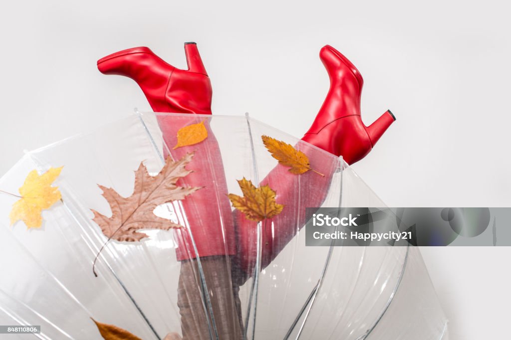 Autumn legs with umbrella Autumn legs in red high boots with umbrella and fallen leaves over light background, focus on legs Boot Stock Photo
