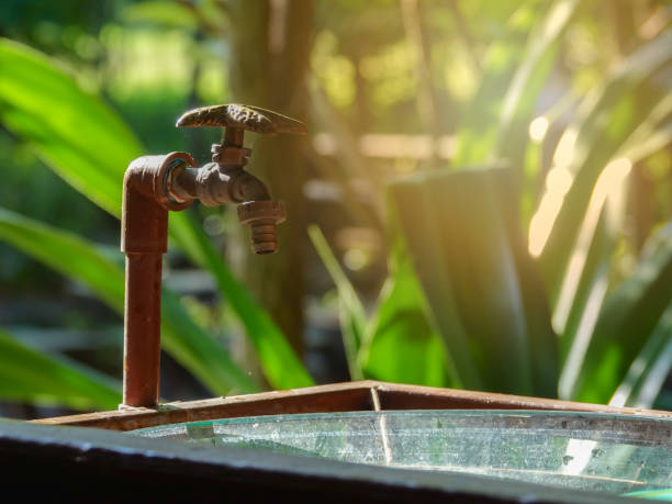 A selective focus of a shiny faucet with an old and rustic pipe against a blurry grass background