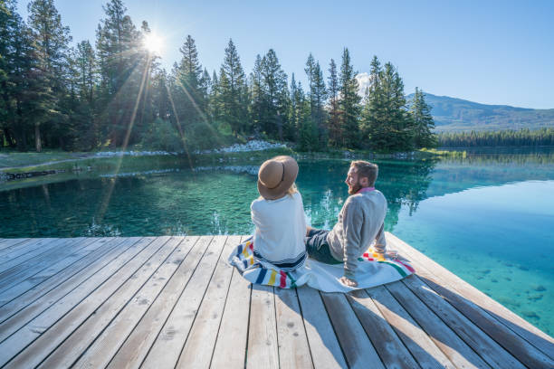 Young couple watching sunrise on lake pier Cheerful young couple sitting on lake pier and sharing some relaxing moments. jasper national park stock pictures, royalty-free photos & images