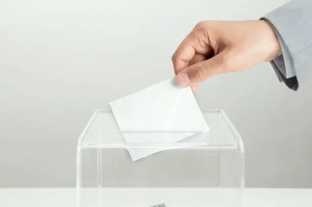 Human hand is inserting empty envelope into election box.