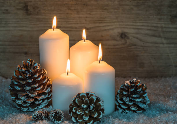 Advent season, four burning Christmas candles with snow and pine cone decoration.
