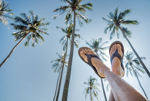 Feet pointing up the clear tropical blue sky with a wonderful palm tree background. Nikon D810. Converted from RAW.