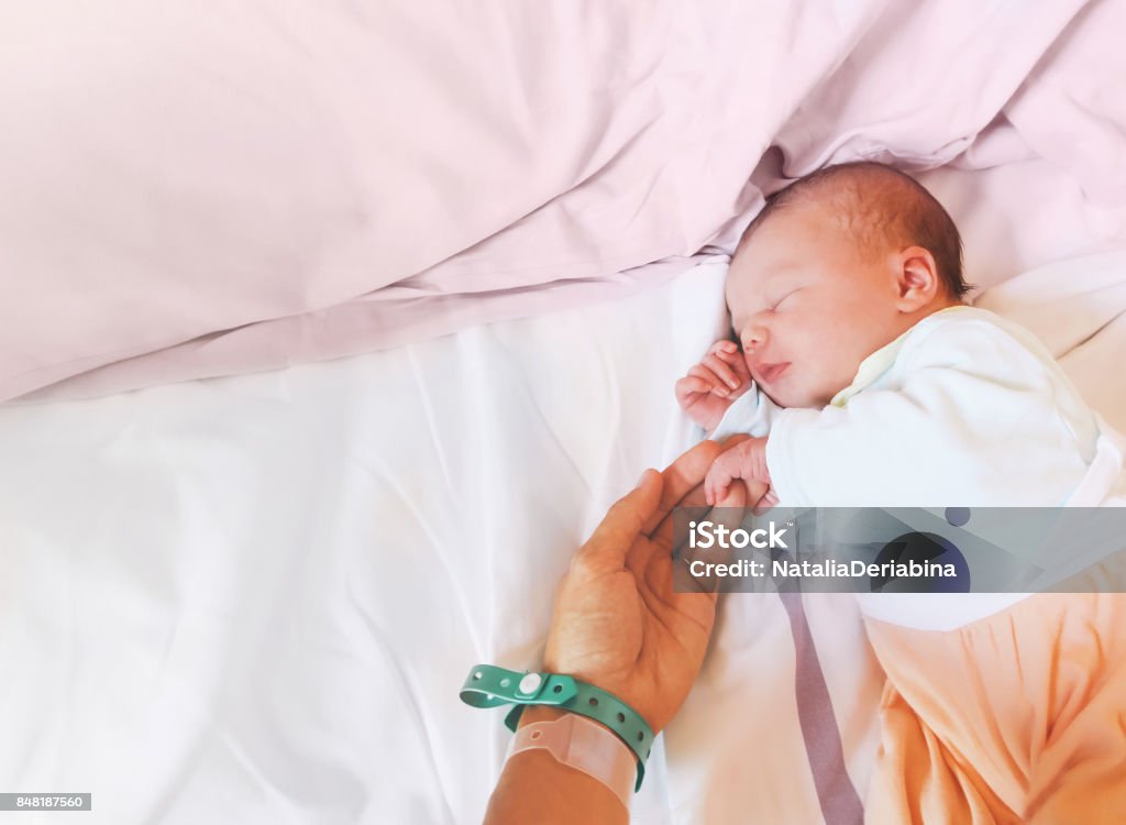 Newborn baby first days of life in delivery room. Newborn baby first days of life in delivery room. Infant asleep in hospital after childbirth. New born and his mother with name tag bracelets. Newborn Stock Photo