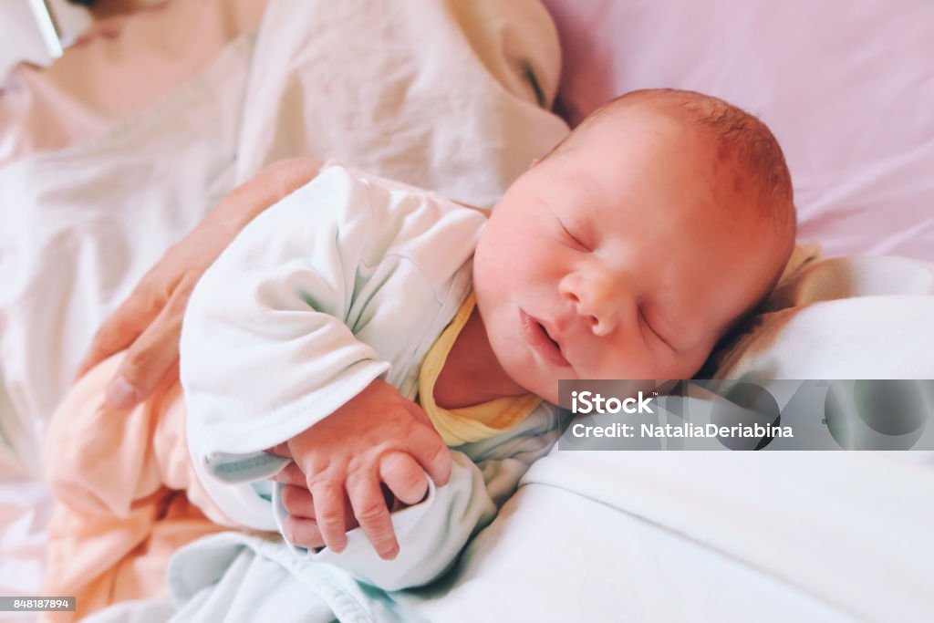 Mother holding her newborn baby child after labor in a hospital. Mother holding her newborn baby child after labor in a hospital. Mother giving birth to a baby. Parent and infant first moments of bonding. Childbirth Stock Photo