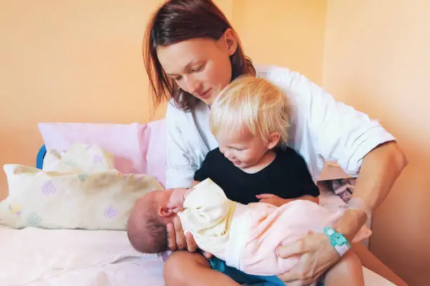 Photo of Mother holding newborn baby with older child in hospital.