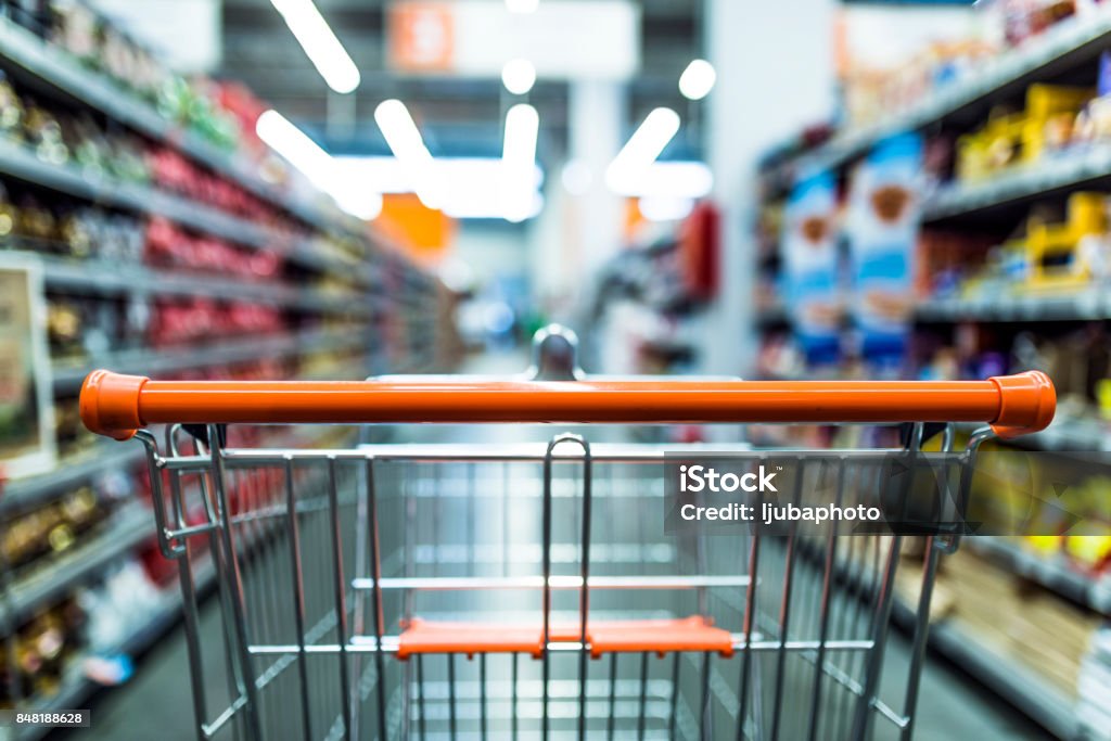 Fast shopping Abstract blurred photo of store with trolley in department store background. Supermarket aisle with empty red shopping cart Shopping Cart Stock Photo