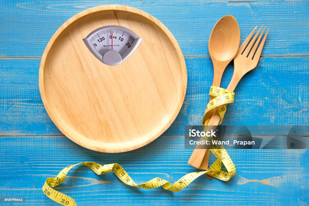 Échelle en forme sur un morceau de bois avec une fourchette et la cuillère, le fond bleu.  Alimentation et santé Concept - Photo de Régime amaigrissant libre de droits