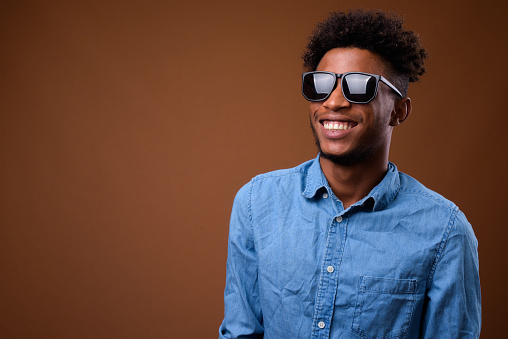 Studio shot of young handsome African man wearing smart casual clothing against colored background horizontal shot