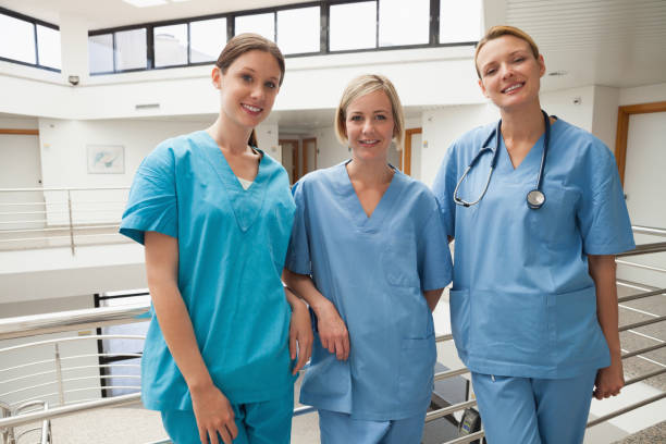Three nurses leaning against railing Three smiling nurses leaning against railing at hospital stairwell Photo of a healthcare team wearing Zuena sustainable scrubs, smiling in a hospital setting stock pictures, royalty-free photos & images