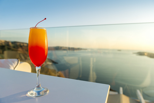 Horizontal color image of Tequila sunrise drink arranged on table with sea view.