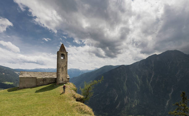 Mountainbiking at the edge of San Romerio, Switzerland. A female mountainbiker is riding nearby the edge of a rock face at Alp San Romerio in front of the scenic little church nearby the village of Poschiavo in the south part of canton Graubünden, Switzerland. The Alp San Romerio with its little church is situated like an eagle´s nest at an altitude of 1793 m (5883 ft.) on top of a rock face overlooking the Poschiavo Valley.
 graubunden canton stock pictures, royalty-free photos & images