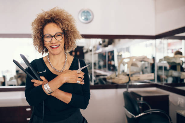 Female hairdresser at the salon holding hairdressing tools Professional hair stylist holding a hair straightener and scissors. Woman hairdresser in happy mood at the salon. alternative pose photos stock pictures, royalty-free photos & images