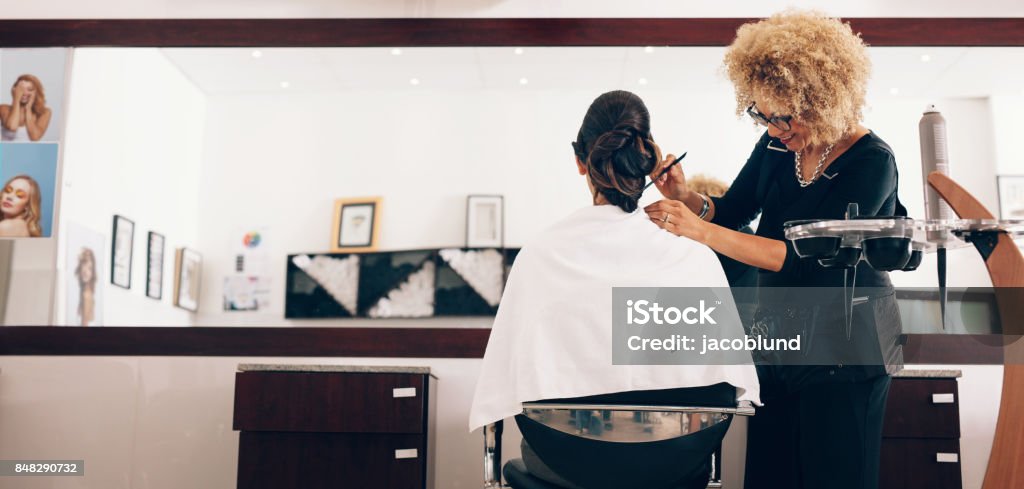 Female hair stylist working on a woman 's hair at salon Hairdresser styling the hair of a customer at salon. Female hair stylist setting hair in fashionable design using a comb. Hairdresser Stock Photo