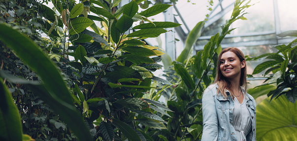 Smiling female working in greenhouse. Young woman standing in plant nursery and smiling.