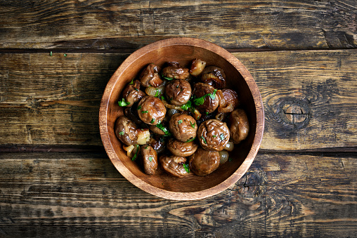 Fried mushrooms with onion in bowl on wooden background, top view