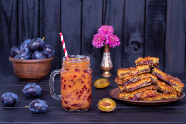 homemade plum pie in plate, plum smoothies and raw plums on black wooden background - plum fruit organic food and drink imagens e fotografias de stock