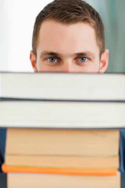 istock Close up of student hiding behind a stack of books 848348580