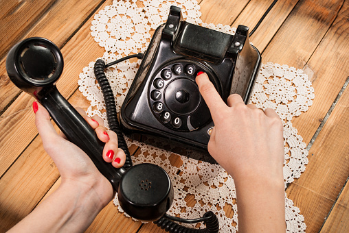 Woman hand dialing number on old phone on lace tablecloths and wooden background. Retro and vintage concept