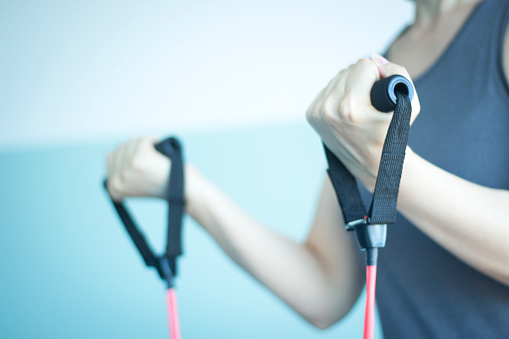 Woman with slim, fit and attractive body in 40's exercising with resistance exercise bands in gym bicep exercise.