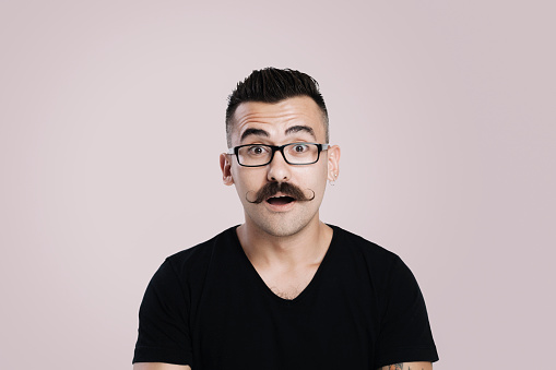 Young male with glasses and mustache, grey background, studio shot, raised eyebrow, surprised, open mouth