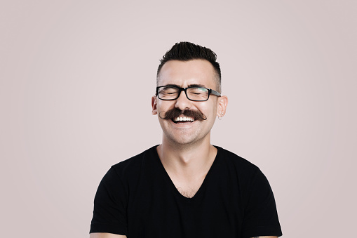 Young male with glasses and mustache, grey background, studio shot, laughing