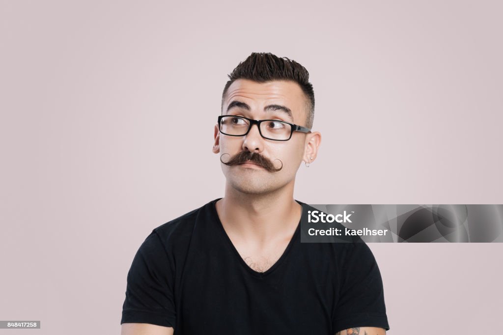 Young man with mustache, thinking and staring into space Young male with glasses and mustache, grey background, studio shot, raised eyebrow Curiosity Stock Photo