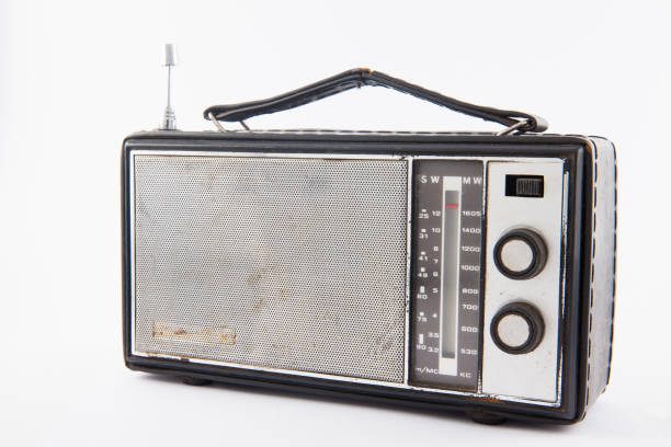 Front view of stylish, retro, portable transistor radio which received FM and AM bands. Radio has a metallic body, analog display, metallic handle, speaker grille with buttons and antenna. Clean image and isolated on white background.