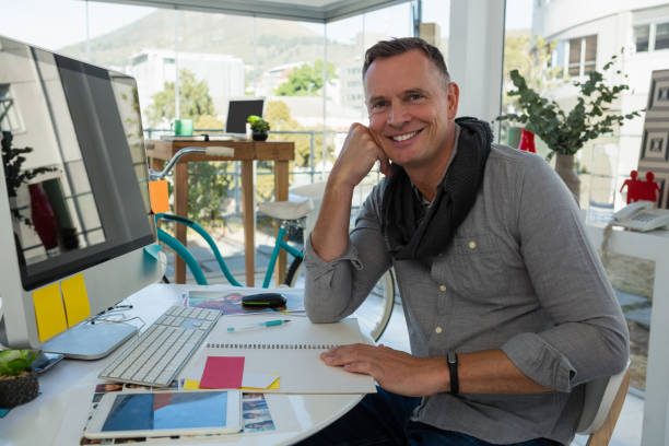 Portrait of smiling businessman sitting at desk Portrait of smiling businessman sitting at desk in studio hhh stock pictures, royalty-free photos & images