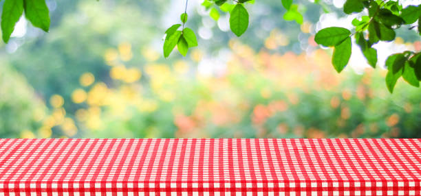 Empty table with red tablecloth over blur green tree and bokeh background, for food and product display montage background, banner