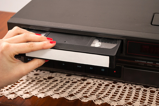 Girl hand inserting blank VHS cassette in old video recorder on doily tablecloth. Retro and Vintage concept