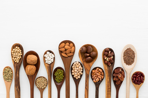 Different kind of beans and lentils in wooden spoon on white wood background. mung bean, groundnut, walnuts, macadamia, almond, soybean, red kidney bean, black bean, sesame, corn, red bean and brown pinto beans