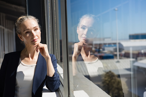 Thoughtful businesswoman with hand on chin looking through window at office