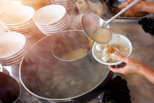 staff making a bowl of noodle with fish ball and pork in local shop restaurant on the street - asian food stock photo