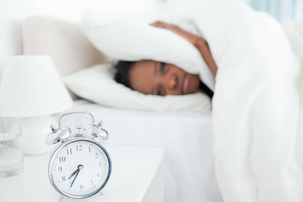 istock Exhausted woman covering her ears while her alarm clock is ringing 848557504