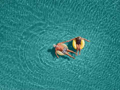 High angle view photo of a senior couple floating in the ocean while using swimming and floating devices